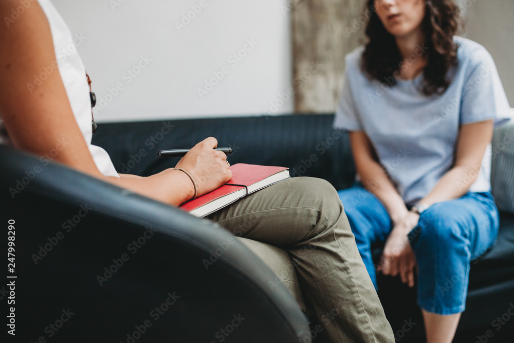 A female therapist with a clipboard and pen talking to a female patient during a session.