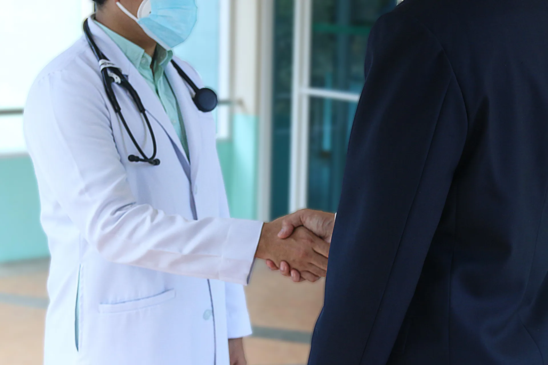 A healthcare professional in a white coat shaking hands with a suited individual, symbolizing a medical practice acquisition deal.